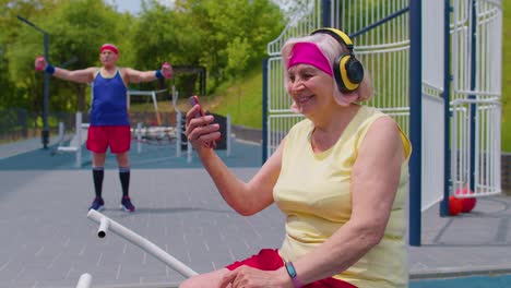 senior woman after sport training listening music from mobile phone wearing headphones on playground