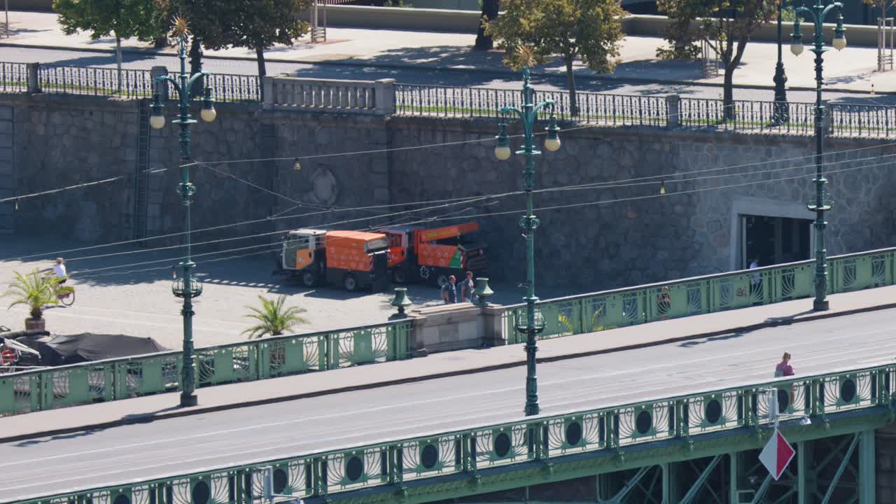 Classic red tram and vehicles travel across city bridge in bright daylight, static elevated perspective