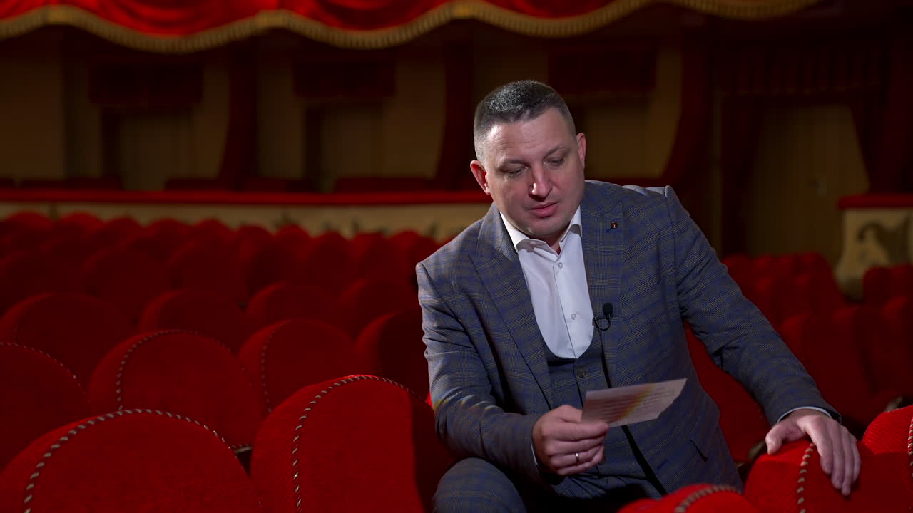 Man in costume reads a script. Medium shot of an actor rehearsing in empty theater among red chairs. Acting lifestyle.