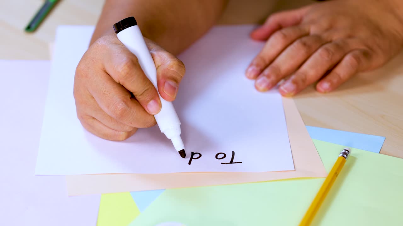 Person writes 'To do list!' with marker on paper, close-up, bright natural lighting