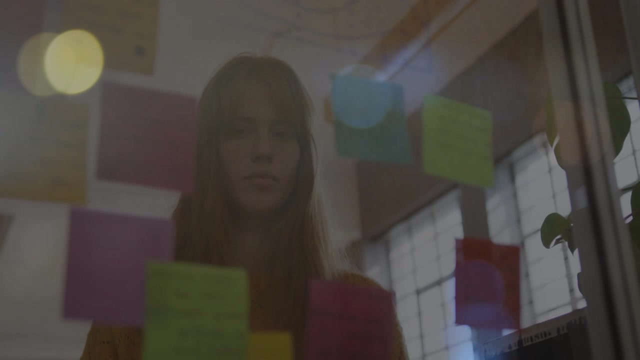 Donna che legge post-it su una superficie di vetro, notando gli appunti superiori e poi spostando lo sguardo verso il basso per la pianificazione