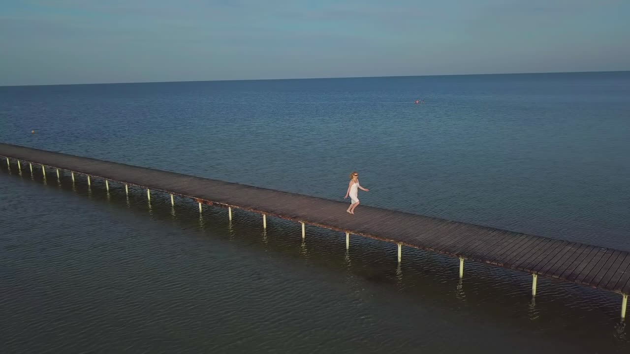 девушка идет по деревянному пирсу рядом с морем 01