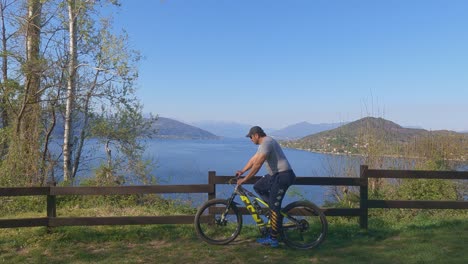 man on bicycle arrives and stops to enjoy amazing panoramic view over maggiore lake, italy