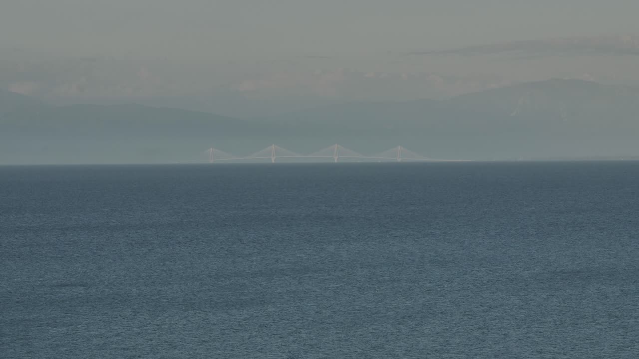 배경에는 산이 있고 전경에는 바다가 있는 멀리 떨어진 다리의 장거리 망원 사진