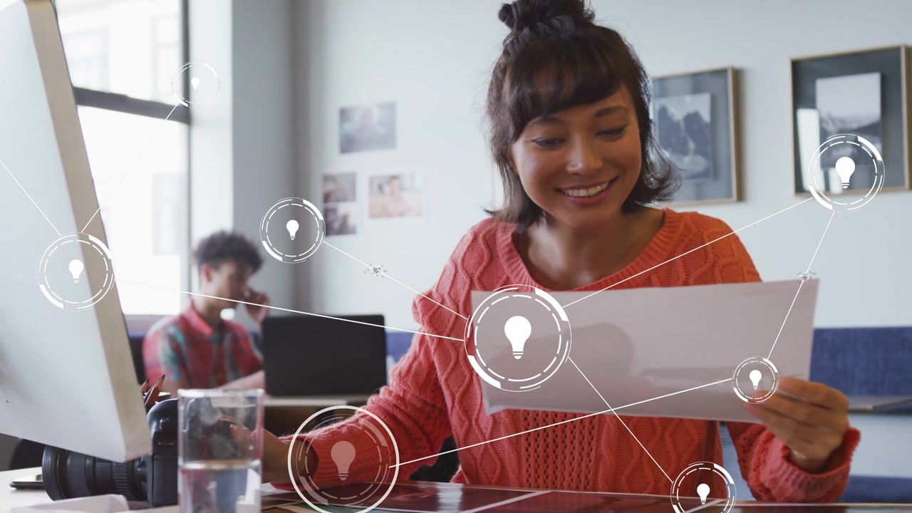 Woman at desk reviewing prints for design with lightbulb overlay appearing, expanding around her