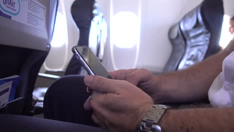 hombre de negocios que viaja en avión usando un teléfono móvil durante el vuelo, desplazándose y escribiendo y haciendo gestos con las manos