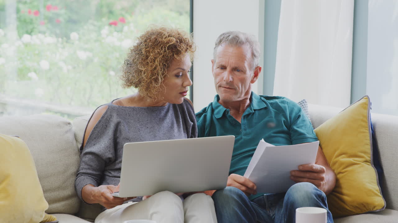 Senior Retired Couple Sitting On Sofa At Home Reviewing Personal Finances On Laptop