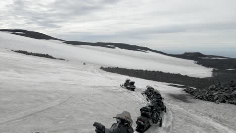 A-drone-sweeps-across-Mount-Katla's-snowy-expanse-in-South-Iceland,-tracking-a-convoy-of-snowmobiles-carving-through-the-pristine-white,-embodying-the-thrill-of-wilderness-exploration