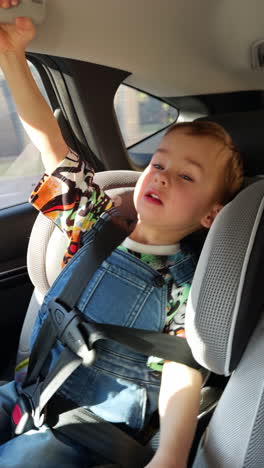 kid sitting in baby car seat holding by the upper handrail. happy child travelling by the city. vertical video.