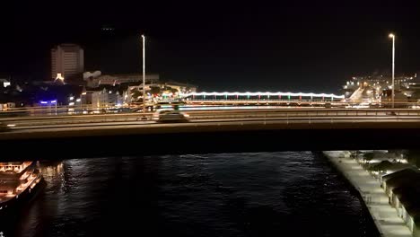 aerial ascend above bridge reveals willemstad curacao at night shimmering lights reflect on water