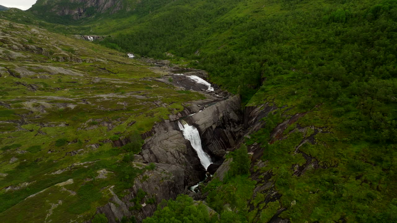 Hiafossen cascades through a rocky valley and green slopes in southwest Norway, left orbit aerial