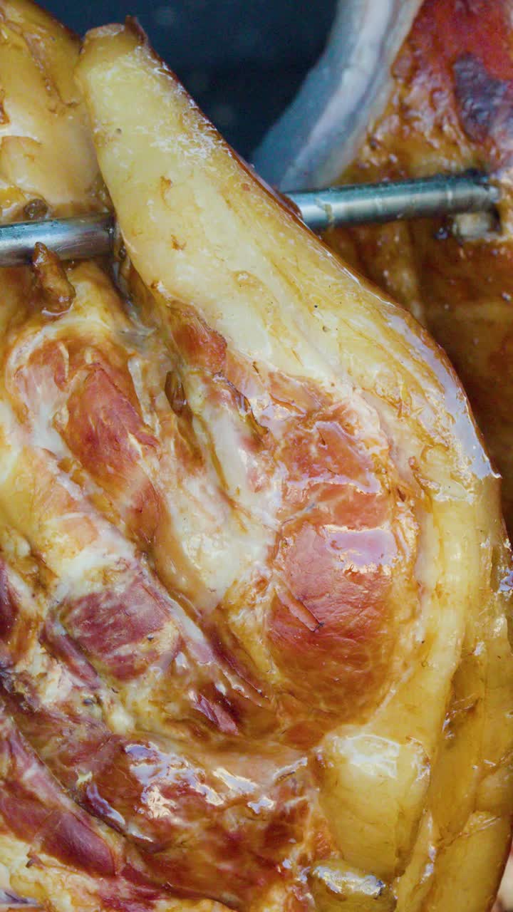 Stinco di maiale succulento che arrostisce lentamente su fuoco a legna aperto, primo piano, luce naturale del giorno, spiedo rotante