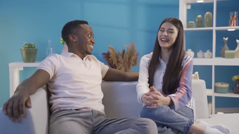 un joven africano feliz y su novia caucásica charlando y sonriendo en casa