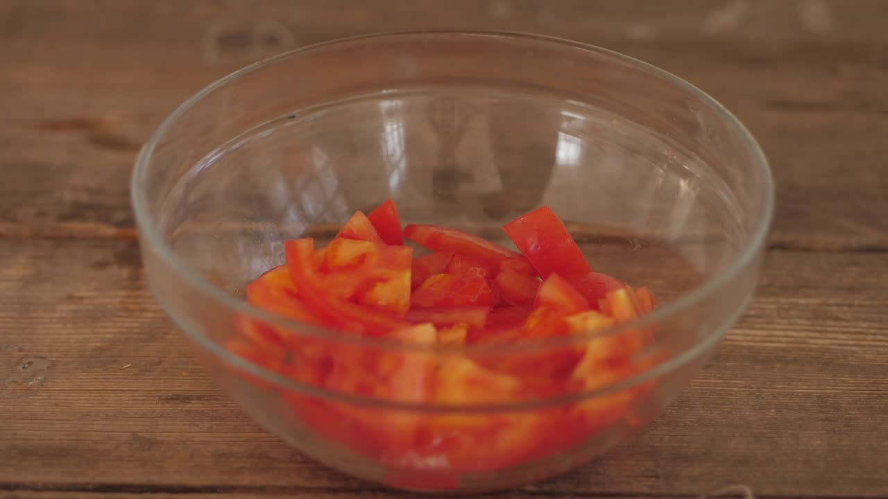 신선한 얇게 썬 토마토 조각이 나무 식탁에 있는 그릇에 담겨 있습니다.