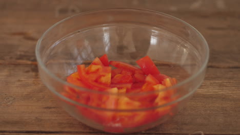 fresh sliced tomato pieces being placed into bowl on wooden kitchen table