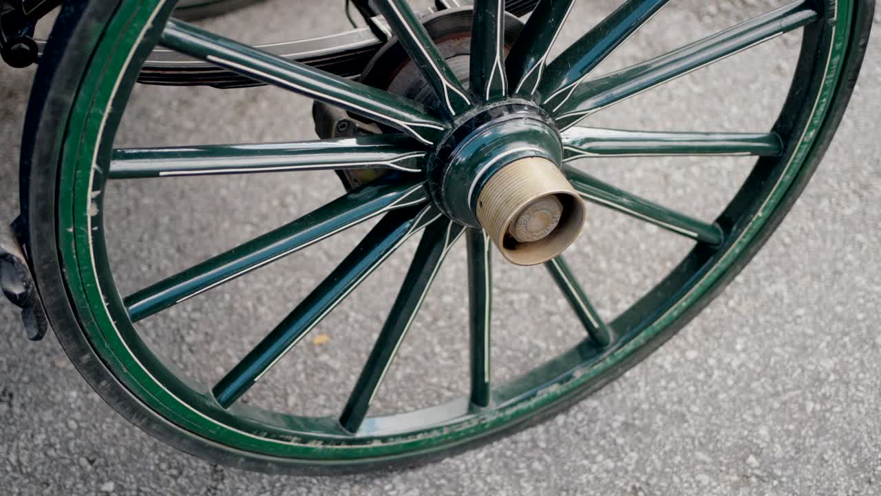 Close-up of a green wooden wheel from a horse-drawn carriage on a paved road.
