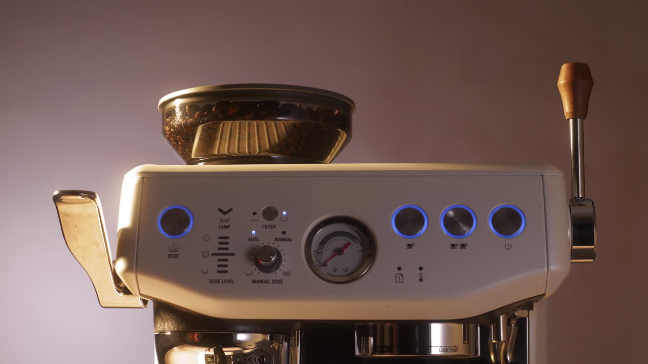 Un primer plano muestra una mano presionando el botón iluminado de una moderna cafetera espresso. El molinillo integrado está lleno de granos de café, destacando el diseño elegante y el inicio del proceso de preparación