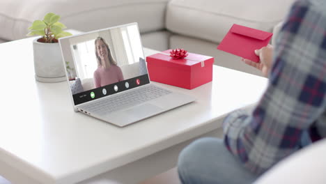 caucasian man holding red envelope using laptop with caucasian woman on screen