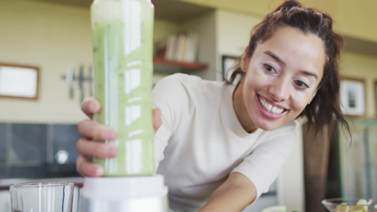 feliz mujer biracial usando licuadora, preparando batido en la cocina
