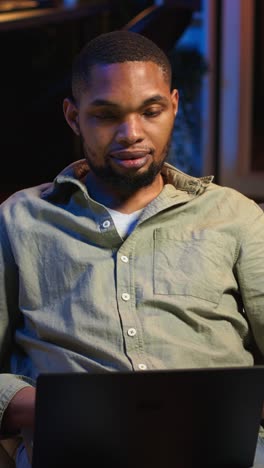 vertical video portrait of african american adult typing data on his laptop at home