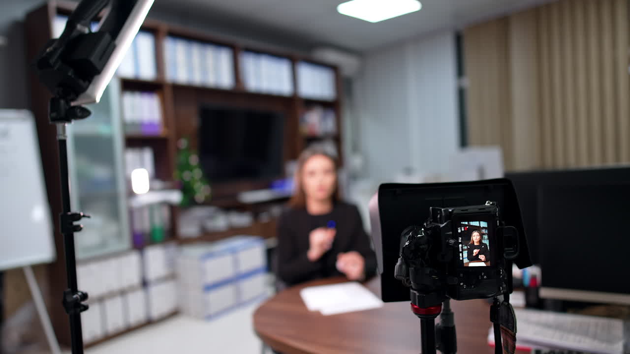 Camera on tripod records a female Caucasian woman. Female blogger talks and gestures with her hands. Blurred backdrop.