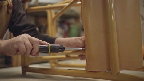 hands of unrecognizable leather craftsman while screwing screws on chair