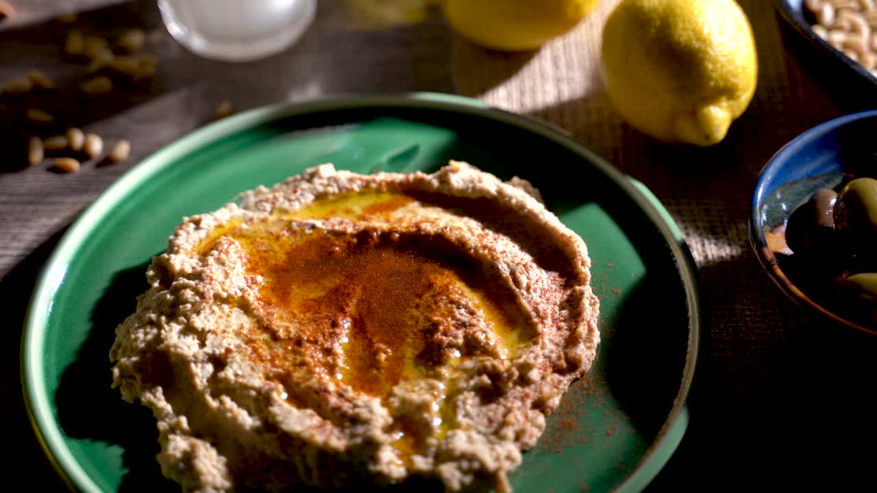 Contrasty, high angle slide to the right of mediterranean food spread with hummus, pine nuts, lemons, olives, get and ouzo or arak