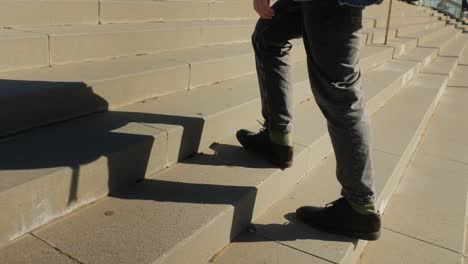 Close-up of a person climbing outdoor stairs during daytime, showcasing their casual pants and shoes.