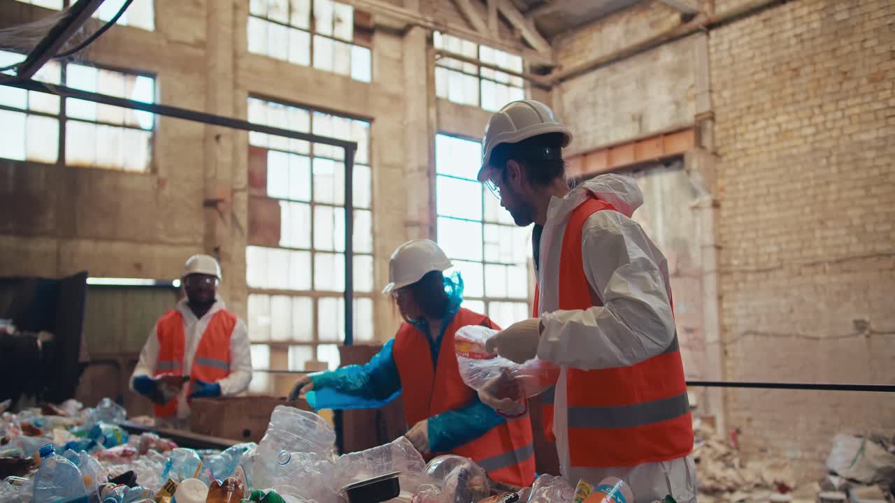 un grupo de tres trabajadores con uniformes blancos y chalecos naranjas reciclan basura y plástico en una cinta transportadora en una planta de reciclaje de residuos. proceso de clasificación de botellas por color en una fábrica de reciclado de residuos