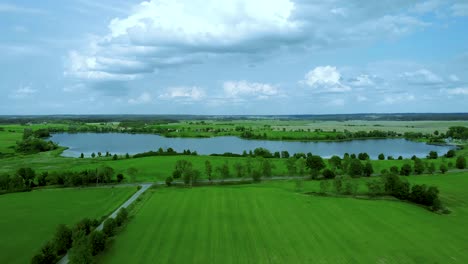 aerial footage over lake, beautiful day near grass field nad road nad pond, high trees and sky with cloud