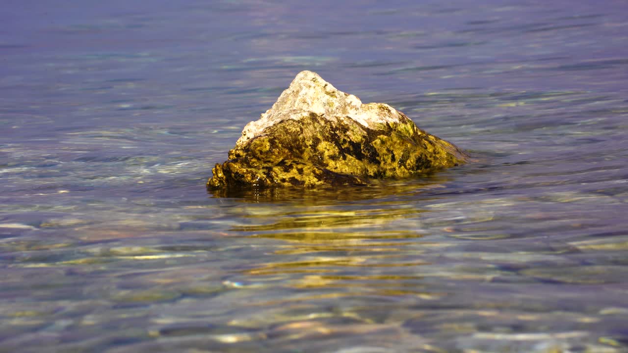 Roccia dorata bagnata dall'acqua del lago in una bella giornata di sole al crepuscolo.