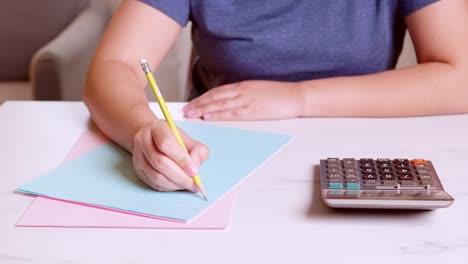 woman is using a calculator to calculate and write down her monthly accounting expenses at home