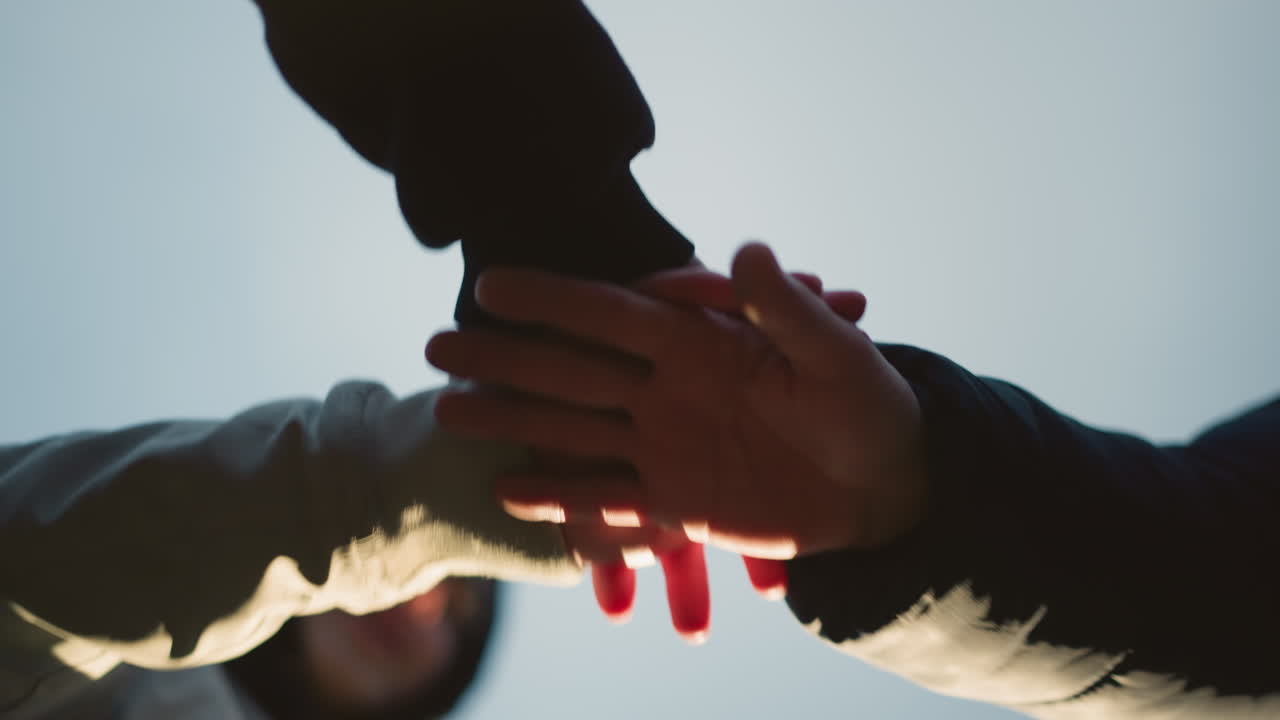 Close-up of three individuals stacking their hands together in a gesture of unity and teamwork against a clear sky background