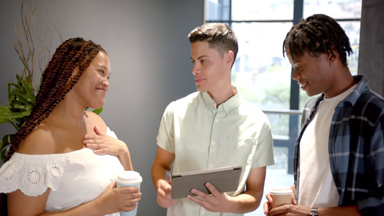 Discussing project, colleagues holding coffee cups and tablet in office setting