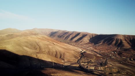 Fuerteventura's-arid-landscape-with-winding-roads-at-sunset,-golden-hour,-aerial-view