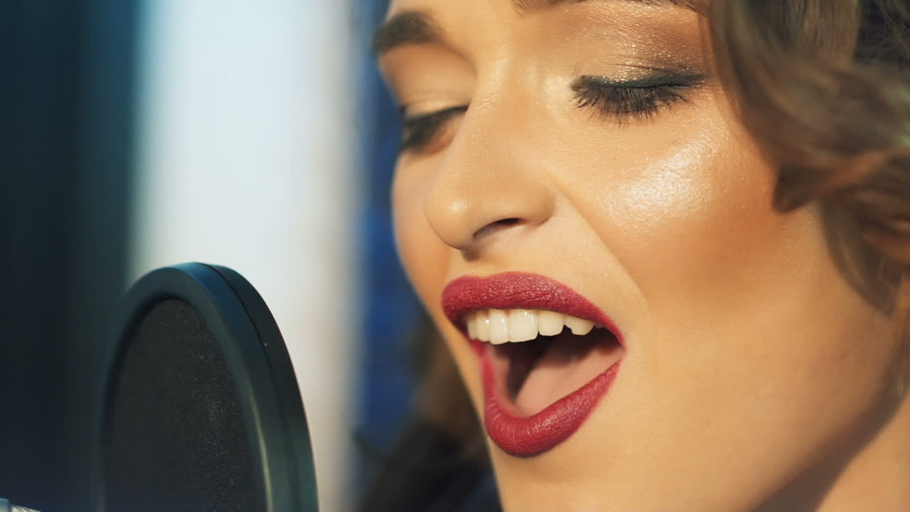 Profile of a beautiful girl's face with perfect makeup singing in the sound studio. Young singer emotionally recording new song. Lady sings into microphone. Slow motion Close-up
