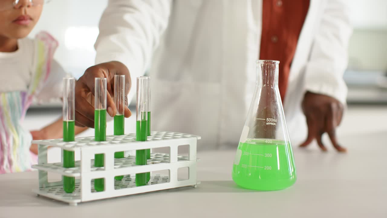 African American teacher lifting flask pointing to rack at lab bench teaching pupil testing