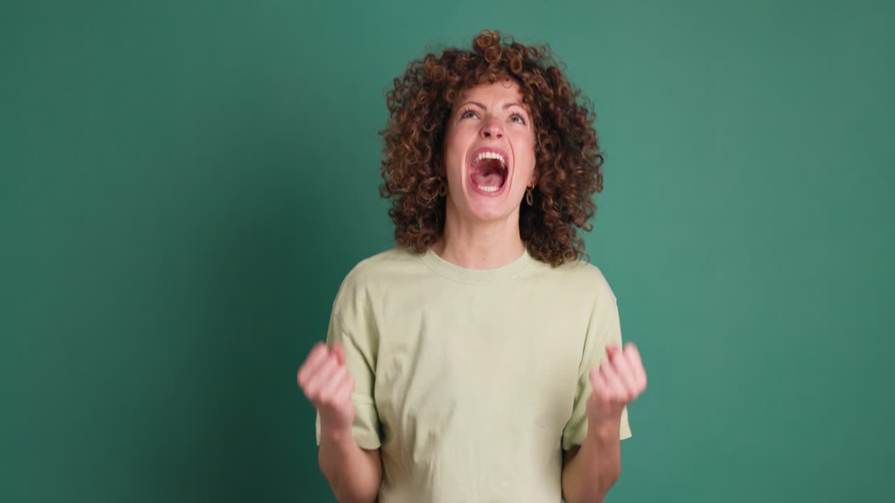 Shocked young woman showing stretched hands with palms on green background
