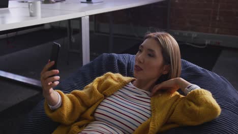 Asian-business-woman-lying-on-bean-bag-taking-selfie-and-smiling-during-break