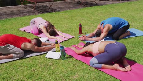 Diverse-group-practicing-yoga,-kneeling-on-mats-and-stretching-in-sunny-park