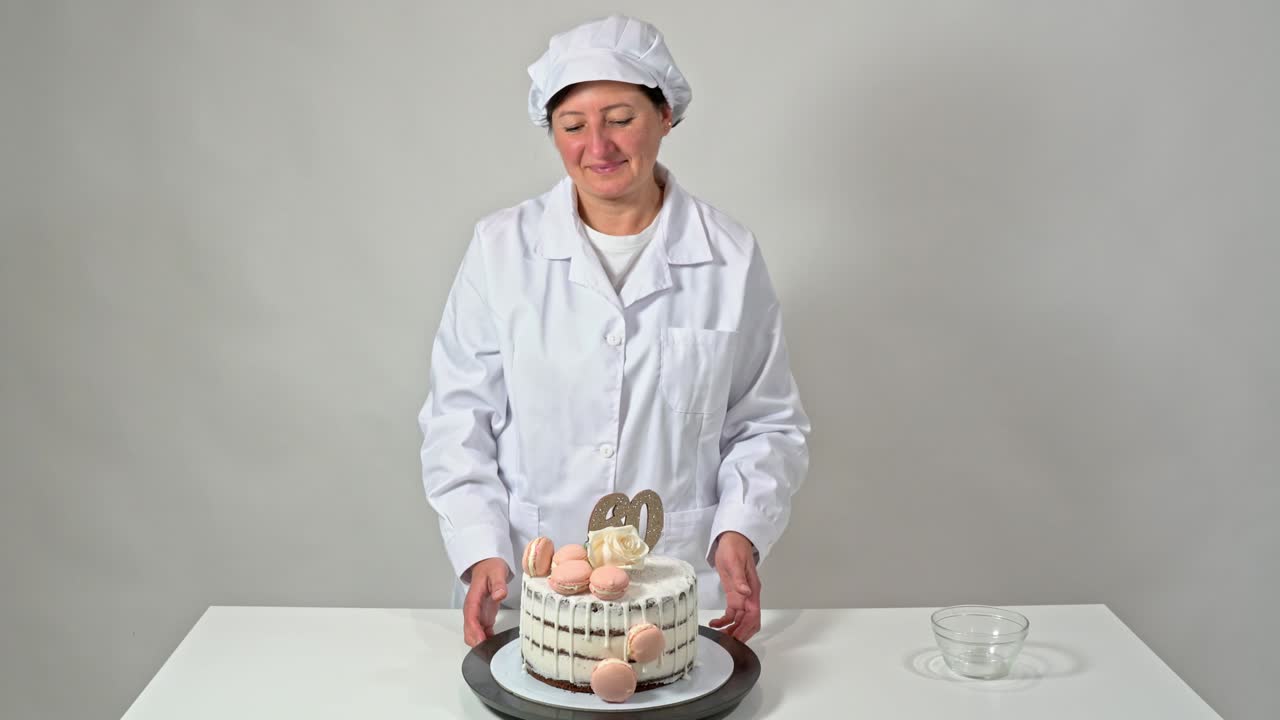 Vakker bursdagskake, dekorert med makroner og en rose, stolt presentert av en kvinnelig baker
