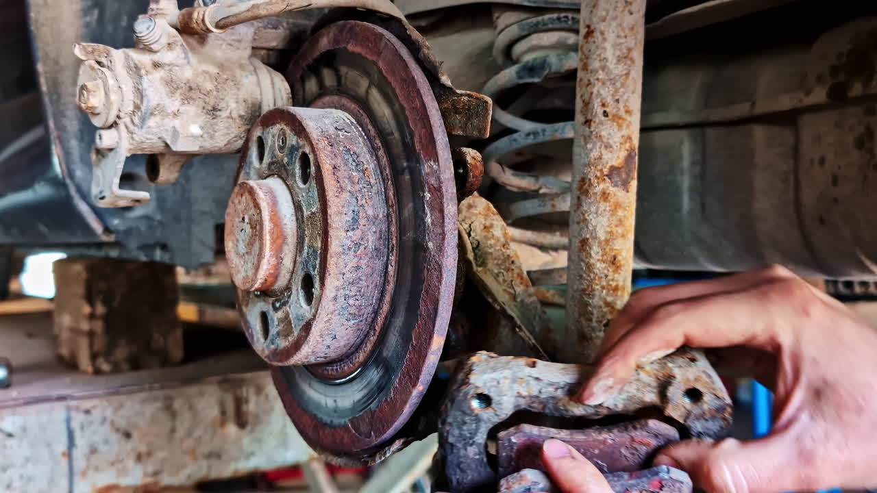 Mechanic removing rare brake caliper from rusted brake disk during repair in workshop