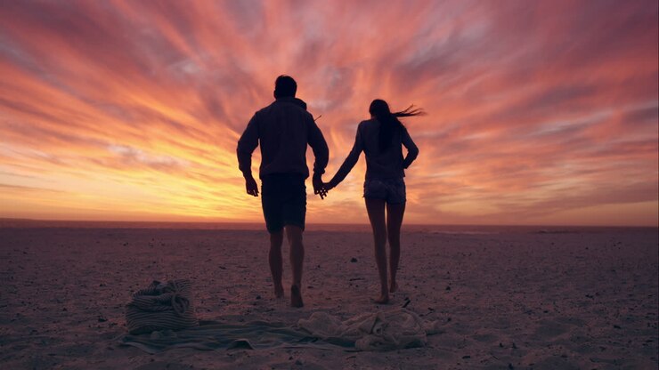 Couple heureux marchant vers le coucher du soleil sur une plage déserte, ciel orange spectaculaire en arrière-plan RED DRAGON