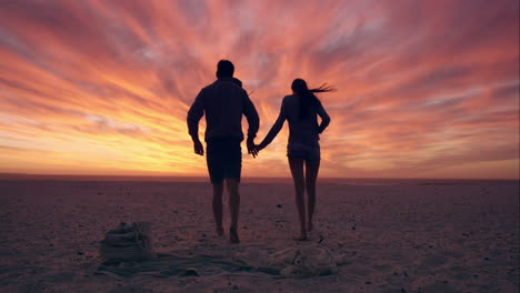 Glückliches-Paar,-Das-Am-Leeren-Strand-Dem-Sonnenuntergang-Entgegengeht,-Dramatischer-Orangefarbener-Himmel-Im-Hintergrund,-Roter-Drache