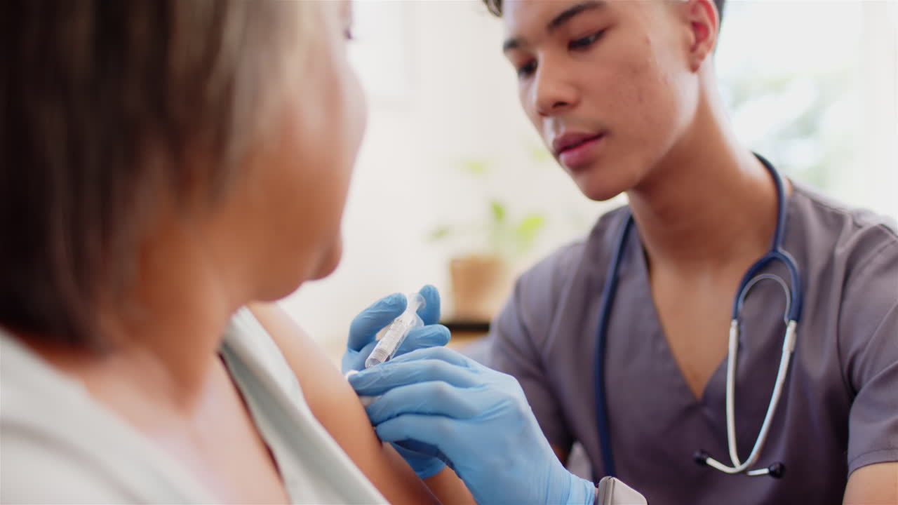 Administering vaccine, male nurse with stethoscope giving injection to senior woman