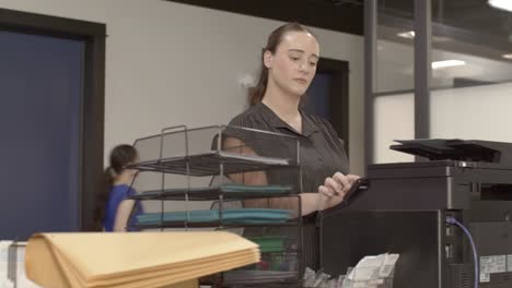 caucasian woman at a printer in a busy office with video moving right to left in front