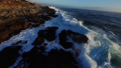 big waves splashing on rocky coast in rough sea, close up fpv aerial view