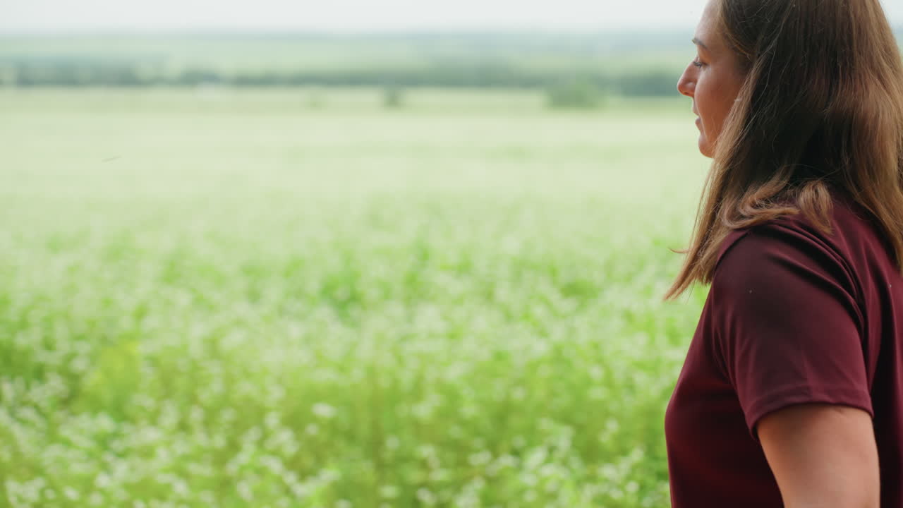 흰색 옷을 입은 여성이 목초지 야외에서 오렌지색 담요를 정리하고 있어요. 홀로 있는 성인이 야생화 들판을 배경으로 천을 매만지며, 사색에 잠긴 표정으로 천천히 신중하게 움직이며 피크닉이나 휴식을 준비하고 있어요.