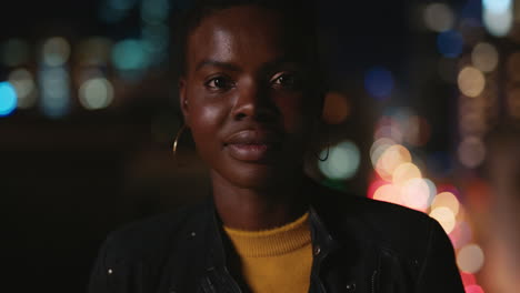 retrato de una hermosa mujer afroamericana en el techo por la noche sonriendo feliz disfrutando de la vida nocturna urbana con luces de la ciudad de bokeh en el fondo