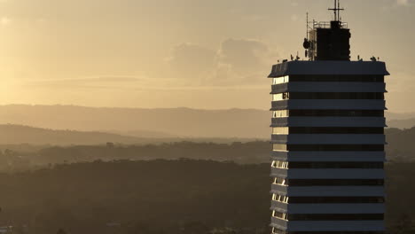 Telephoto-Panning-Drone-Parallax-High-Rise-Building-Overlooking-Hinterland-Mountains-At-Sunset,-Drone-4K